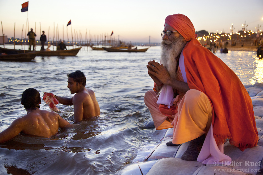 India. Uttar Pradesh state. Allahabad. Maha Kumbh Mela. Two Indian Hindu devotees take a holy dip and a sanyasi prays in Sangam at the sunset. The old saint man wears saffron clothes. Sanyasis, or renunciates, have left behind all material attachments. They are renouncers who have chosen to live a life apart from or on the edges of society in order to focus on their own spiritual practice. The Kumbh Mela, believed to be the largest religious gathering is held every 12 years on the banks of the 'Sangam'- the confluence of the holy rivers Ganga, Yamuna and the mythical Saraswati. In 2013, it is estimated that nearly 80 million devotees took a bath in the water of the holy river Ganges. The belief is that bathing and taking a holy dip will wash and free one from all the past sins, get salvation and paves the way for Moksha (meaning liberation from the cycle of Life, Death and Rebirth). Bathing in the holy waters of Ganga is believed to be most auspicious at the time of Kumbh Mela, because the water is charged with positive healing effects and enhanced with electromagnetic radiations of the Sun, Moon and Juppiter. The Maha (great) Kumbh Mela, which comes after 12 Purna Kumbh Mela, or 144 years, is always held at Allahabad. Uttar Pradesh (abbreviated U.P.) is a state located in northern India. 7.02.13 © 2013 Didier Ruef *** Local Caption ***